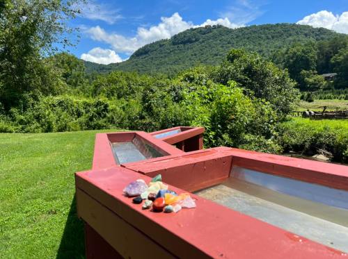 A sunny landscape featuring a red wooden structure with colorful stones, set against a backdrop of green mountains.