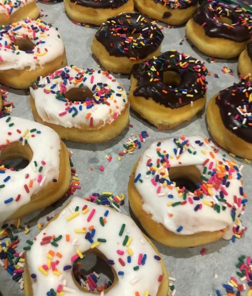 A variety of donuts with white and chocolate icing, topped with colorful sprinkles, arranged on a tray.