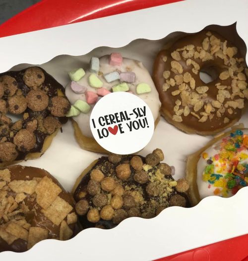 A box of colorful donuts topped with cereal, featuring a card that says, "I CEREAL-SLY LOVE YOU!"