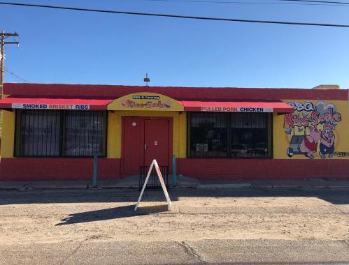 Colorful BBQ restaurant exterior with signs for smoked brisket ribs and pulled pork chicken. Bright red door and awnings.