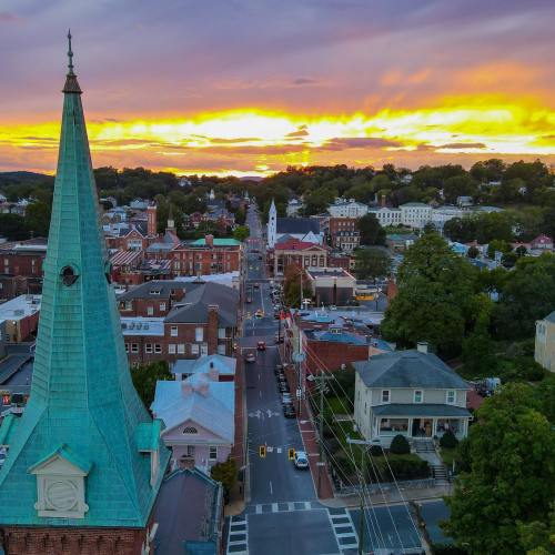 Aerial view of a town at sunset, featuring a church steeple, streets, and colorful sky with clouds.