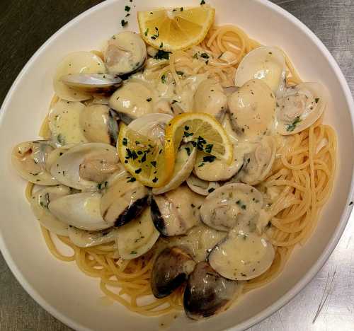 A bowl of spaghetti topped with clams in a creamy sauce, garnished with lemon slices and parsley.