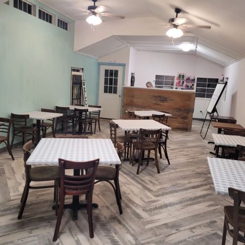 A spacious, light-colored room with tables and chairs, featuring a wooden counter and a whiteboard.