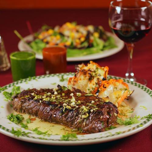 A juicy steak garnished with herbs, served with grilled vegetables and sauces, alongside a glass of red wine.