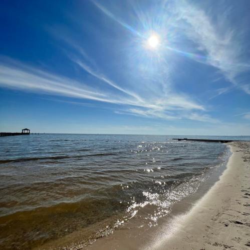 A serene beach scene with calm waters, gentle waves, and a clear blue sky with wispy clouds.