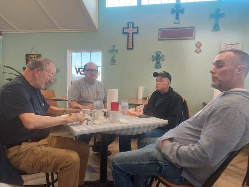 Four men sit around a table in a casual dining setting, engaged in conversation and enjoying their meal.