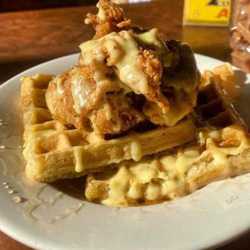 A plate of waffles topped with crispy fried chicken and drizzled with creamy sauce.