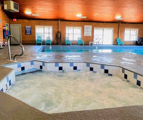 Indoor pool area featuring a hot tub, blue water, and lounge chairs under a wooden ceiling.
