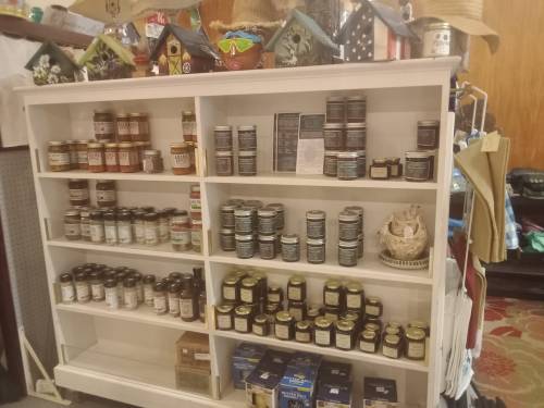 A white shelf displaying various jars and cans of products, including preserves and other items, in a store setting.