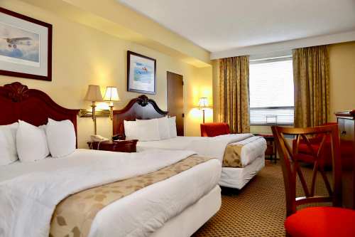A cozy hotel room featuring two beds, a desk, and warm lighting with curtains and artwork on the walls.