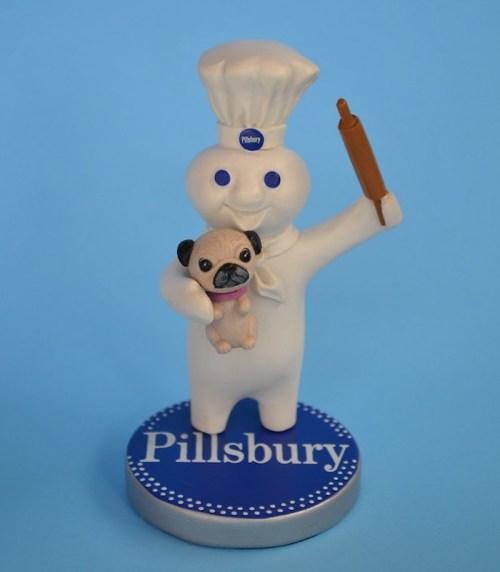A smiling Pillsbury Doughboy figurine holding a rolling pin and a small pug dog, set against a blue background.
