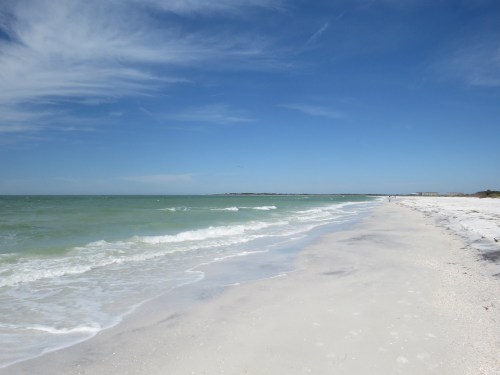 A serene beach scene with gentle waves, soft white sand, and a clear blue sky.