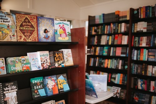 A cozy bookstore interior featuring shelves of colorful books and a display of children's titles in the foreground.