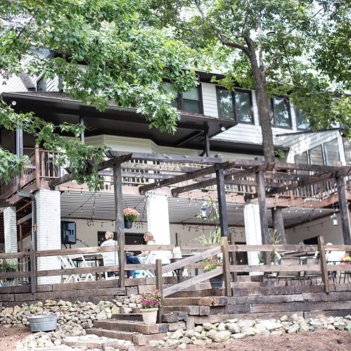 A spacious outdoor deck area with seating, surrounded by trees and a stone pathway leading to a house.