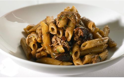 A bowl of penne pasta topped with a rich, savory sauce and garnished with herbs.
