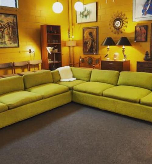 A bright yellow-green sectional sofa in a cozy room with yellow walls and various artworks and lamps.