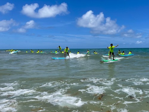 A group of surfers in bright yellow shirts riding waves in a sunny ocean setting.