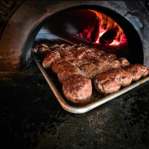 A tray of freshly cooked meatballs sits in front of a glowing wood-fired oven.
