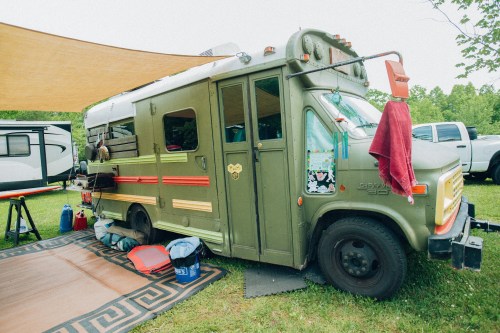A vintage green camper van parked on grass, with outdoor gear and a shaded area set up nearby.