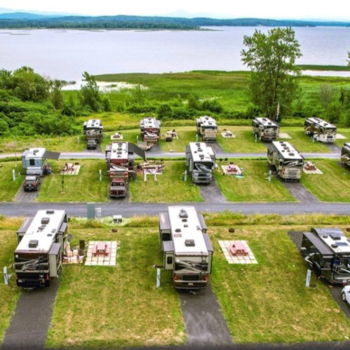 Aerial view of a campground with several RVs parked near a lake, surrounded by greenery and picnic areas.