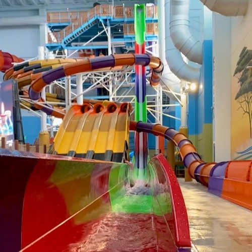 Colorful water slides in an indoor water park, with a splash pool at the bottom and a bright, fun atmosphere.