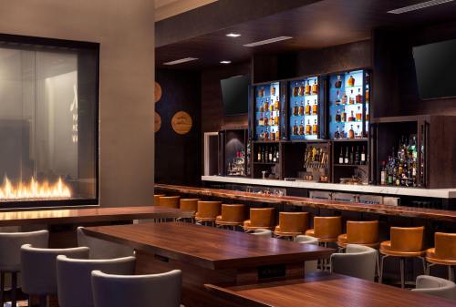 A modern bar interior featuring a sleek counter, high stools, and a wall of illuminated liquor bottles.