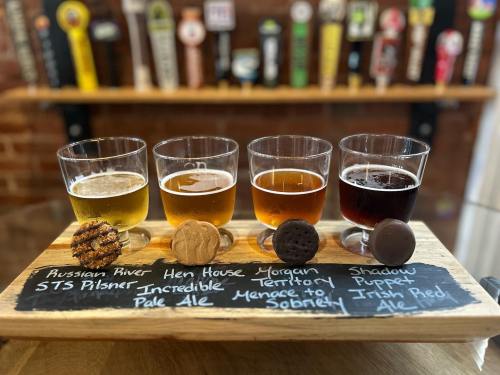 A flight of five craft beers paired with cookies on a wooden board, labeled with their names and styles.