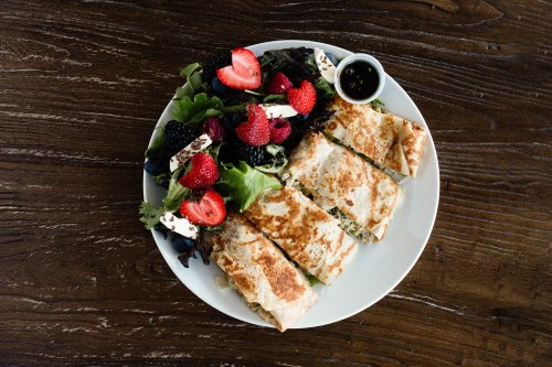 A plate with sliced quesadillas and a fresh salad topped with strawberries, raspberries, and a small dressing cup.