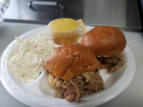 Two pulled pork sliders on a plate with coleslaw and a cornbread muffin.