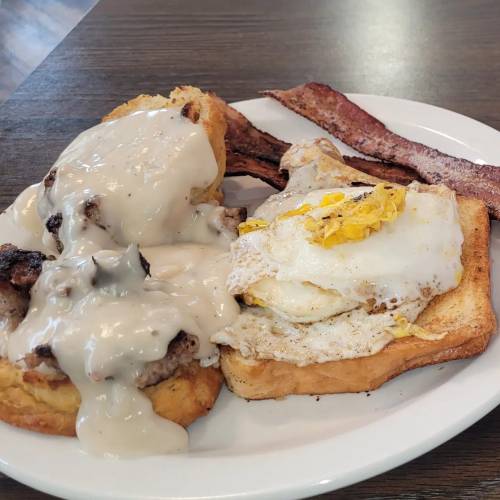 A plate featuring two pieces of toast topped with sausage gravy, an egg, and crispy bacon on the side.