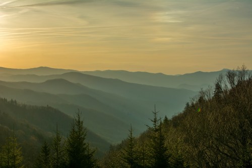 A serene landscape of rolling mountains at sunset, with soft hues and mist creating a tranquil atmosphere.