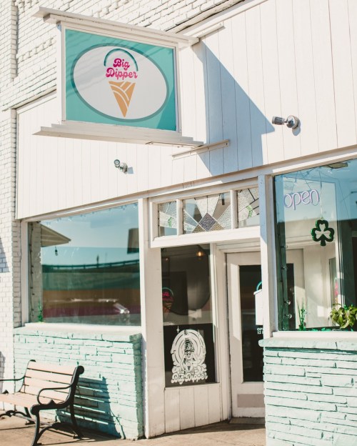 Exterior of Big Dipper ice cream shop, featuring a colorful sign and open window, with a bench outside.