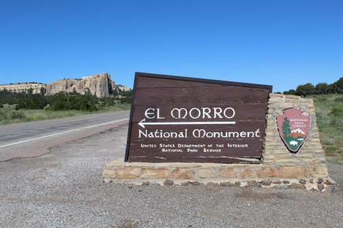 Sign for El Morro National Monument, with a rocky formation in the background and clear blue sky above.