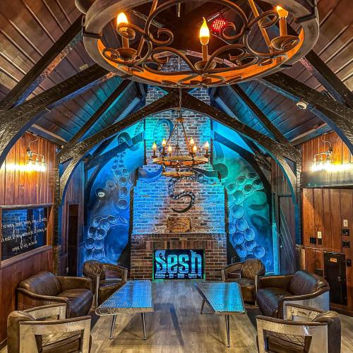 Cozy interior with wooden beams, a brick wall featuring octopus art, and stylish seating under a chandelier.