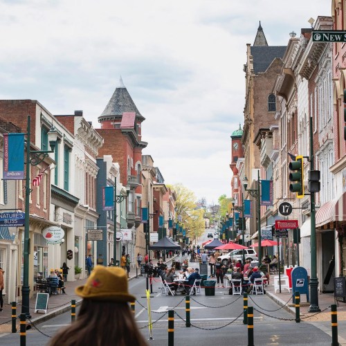 A bustling street scene with shops, outdoor seating, and people enjoying a lively atmosphere under cloudy skies.