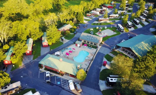 Aerial view of a campground featuring a pool, cabins, and RVs surrounded by greenery.
