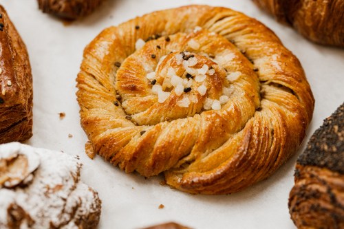 A golden, spiral pastry topped with sugar crystals, surrounded by various baked goods on parchment paper.
