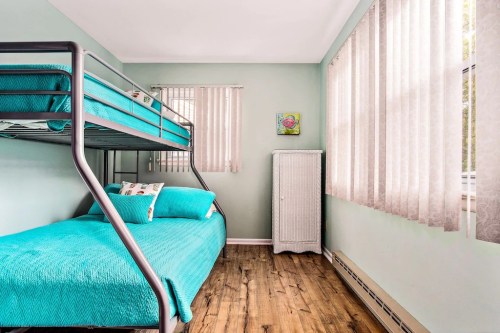 A cozy bedroom with a bunk bed, turquoise bedding, light wood flooring, and sheer curtains letting in natural light.