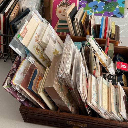 A wooden box filled with assorted cards, stationery, and craft supplies, surrounded by various decorative items.