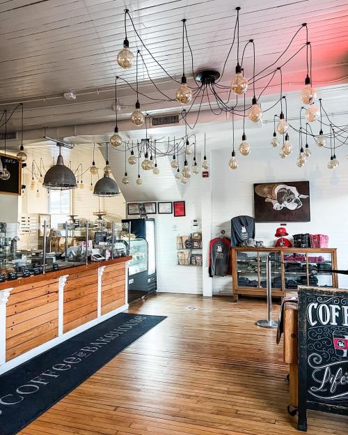 Cozy coffee shop interior with wooden counter, hanging light bulbs, and display cases. Warm, inviting atmosphere.