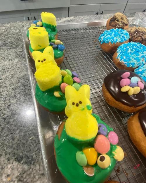 Colorful donuts topped with green icing, marshmallow chicks, and candy eggs, arranged on a cooling rack.