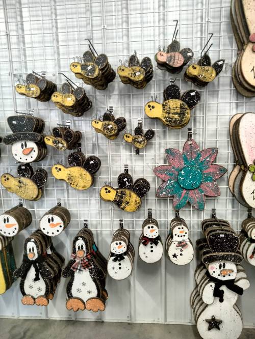 A display of wooden decorations featuring snowmen, penguins, bees, and a colorful flower, hanging on a grid wall.