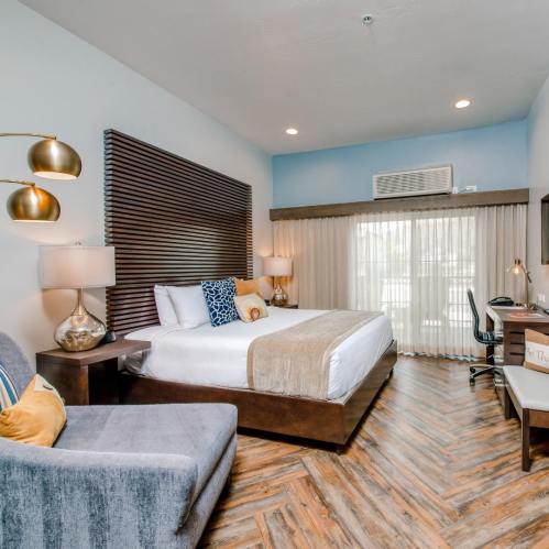 Modern hotel room featuring a king bed, stylish decor, a seating area, and large windows with natural light.