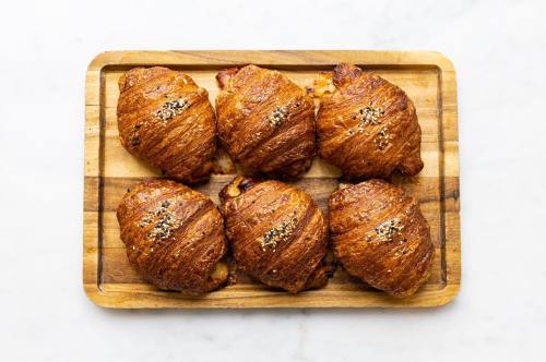 A wooden tray holds six golden-brown croissants topped with sesame seeds.