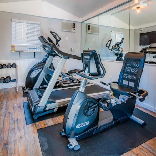 A modern gym with exercise equipment, including a stationary bike and elliptical, set in a bright, mirrored room.