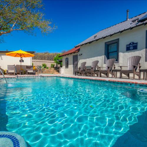 A clear blue pool with lounge chairs and an umbrella, surrounded by a sunny outdoor area and a charming building.