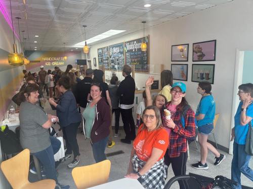 A busy ice cream shop filled with people enjoying treats and socializing, with colorful decor and a cheerful atmosphere.