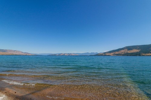A serene lake with clear blue water, surrounded by mountains under a bright blue sky.