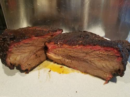 A sliced brisket with a dark, smoky crust and tender, juicy interior, resting on a white cutting board.