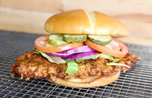 A crispy fried chicken sandwich topped with lettuce, tomato, pickles, and onions on a soft bun.